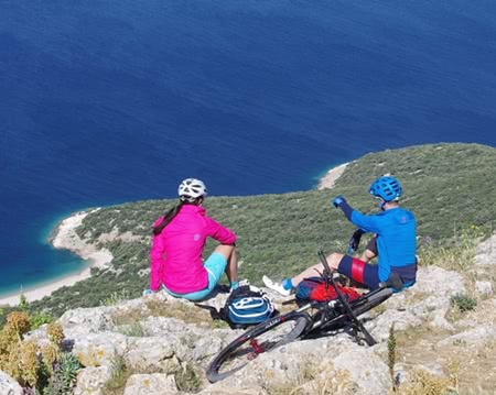 Two people sitting on rocky outcrop with coast and sea in the background